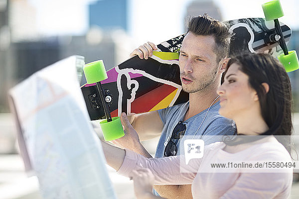 Junges Paar mit Skateboard schaut auf Stadtplan