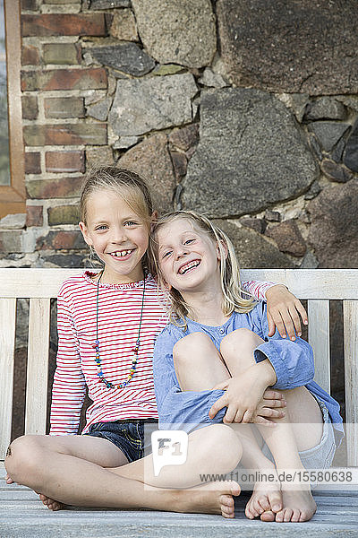 Porträt von zwei lächelnden Mädchen auf einer Bank sitzend