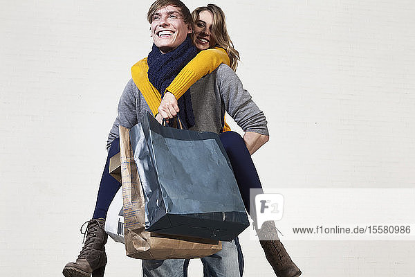 Deutschland  Bayern  München  Junger Mann trägt Frau auf dem Rücken  während sie Einkaufstüten hält