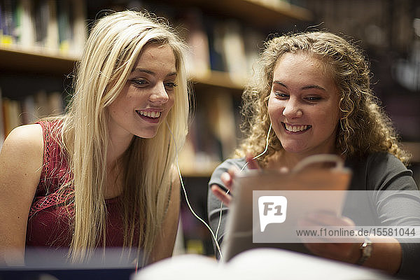 Two female students with digital tablet in a library
