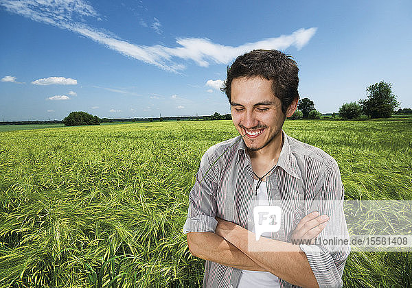 Deutschland  Junger Mann mit verschränkten Armen im Feld  lächelnd