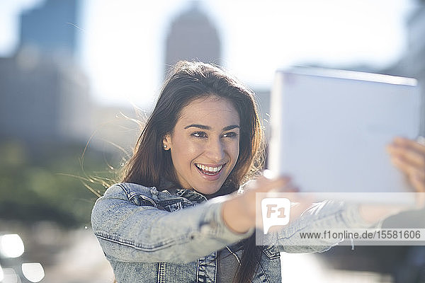 Porträt einer glücklichen jungen Frau  die sich mit einem digitalen Tablett ein Selfie gönnt