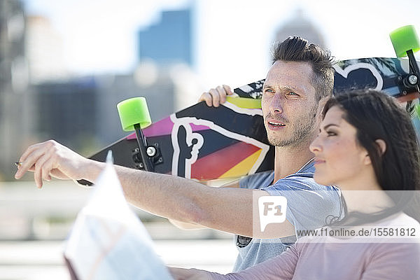 Junges Paar mit Skateboard und Stadtplan in der Ferne