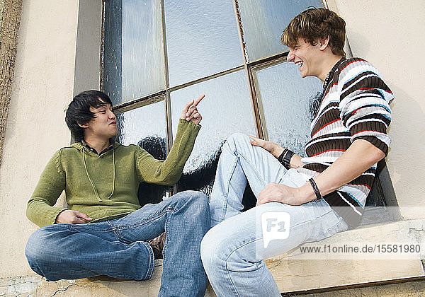 Deutschland  Zwei Freunde sitzen auf dem Fensterbrett und lachen