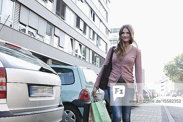 Deutschland  Köln  Junge Frau mit Einkaufstaschen  lächelnd  Portrait