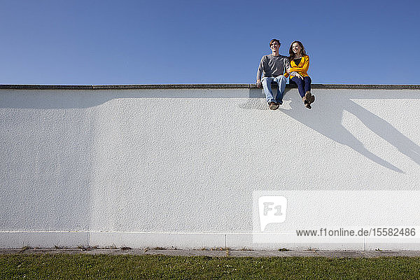 Germany  Bavaria  Munich  Young couple sitting on wall  smiling