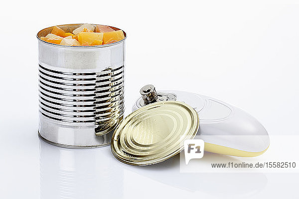 Tropische Früchte in Dose mit elektrischem Dosenöffner auf weißem Hintergrund