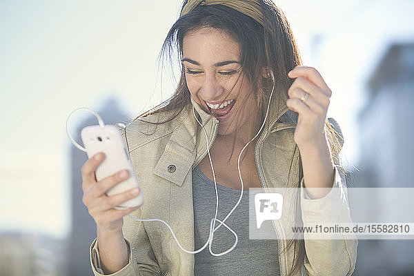 Porträt einer lachenden Frau mit Smartphone und Kopfhörern beim Musikhören