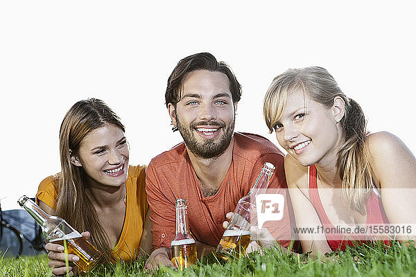 Germany  Cologne  Young man and woman lying in grass with beer bottles  smiling