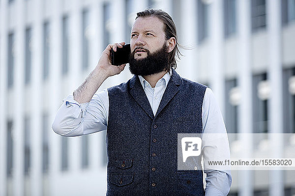 Porträt eines bärtigen Geschäftsmannes mit Weste am Telefon
