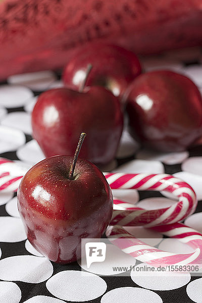 Rote Äpfel und rot-weiße Zuckerrohre auf gemustertem Tuch