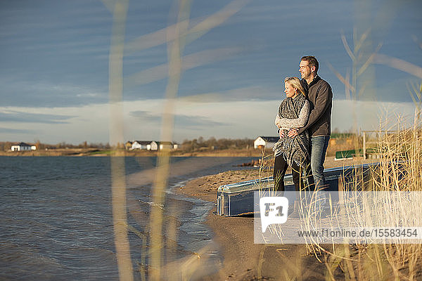 Glückliches Paar steht am Seeufer und umarmt sich