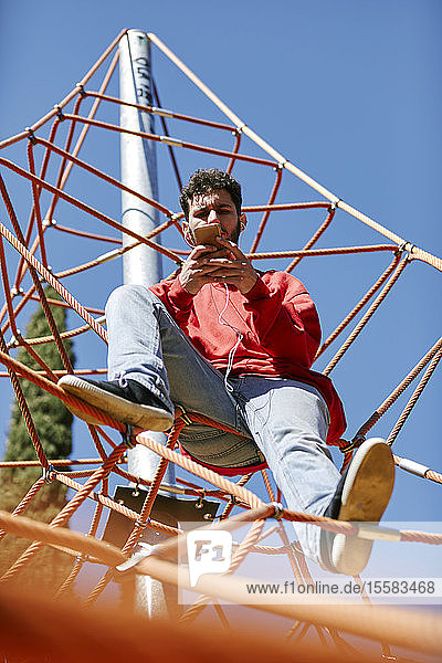 Young man using cell phone on a climbing frame on a playground