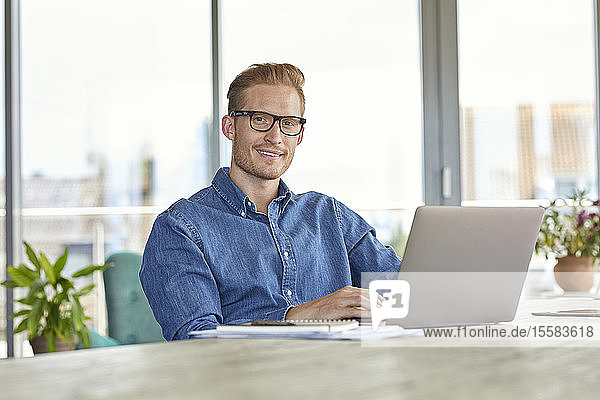 Portrait of smiling young man sitting at table using laptop
