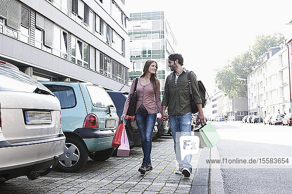 Germany  Cologne  Young couple with shopping bags near parking lot  smiling