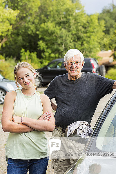Senior man  grandfather and his 13 year old grand daughter washing a car together in driveway
