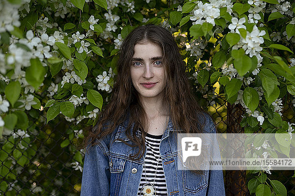 Young woman wearing denim jacket by white flowers