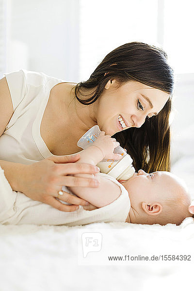 Mutter beobachtet ihren kleinen Jungen beim Trinken von Milch aus der Flasche