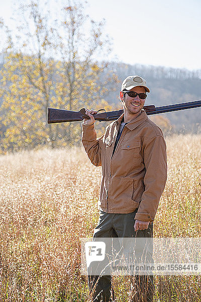 Lächelnder junger Mann mit Gewehr im Feld