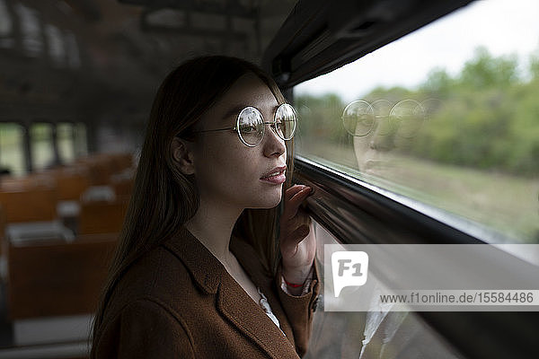 Young woman wearing glasses looking out of train window