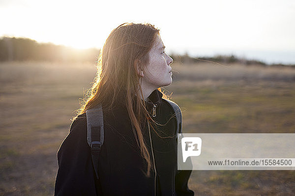 Teenage girl wearing backpack in field at sunset