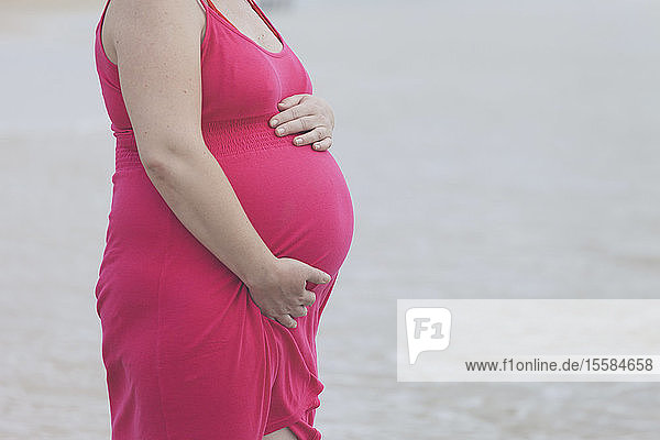Schwangere Frau im rosa Kleid am Strand