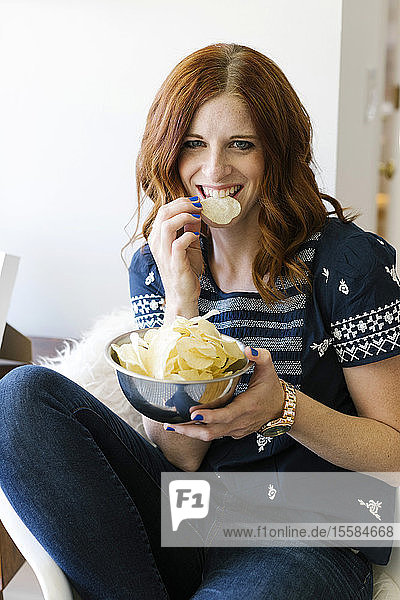 Lächelnde Frau isst Chips aus einer Schüssel