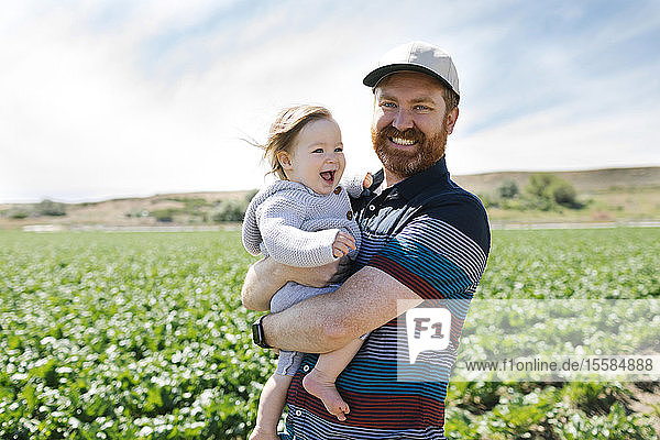 Smiling father holding baby girl in crop field