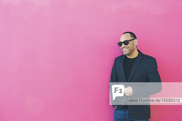 Lächelnder Mann mit Sonnenbrille und Blazer an einer rosa Wand