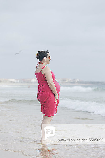 Schwangere Frau im rosa Kleid am Strand