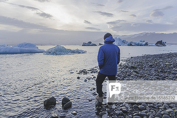 Mann in blauem Mantel am Gletschersee Jokulsarlon in Island