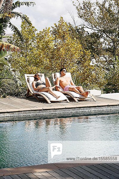 Junges Paar entspannt auf Liegestuhl am Schwimmbad