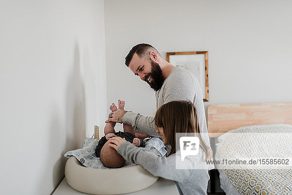 Junger Mann und Tochter beim Wickeln der Windel des Sohnes im Schlafzimmer  Seitenansicht