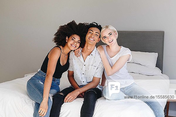 Happy young man and two female friends sitting on bed  portrait