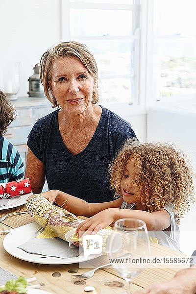 Frau mit Enkelin spielt mit Weihnachtsgebäck am Esstisch
