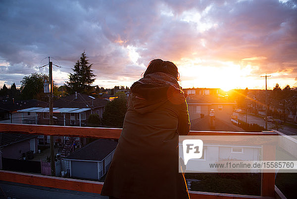 Mittlere erwachsene Frau  die vom Balkon auf den Sonnenuntergang schaut  Rückansicht  Vancouver  British Columbia  Kanada