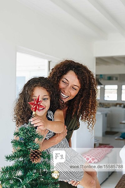 Mutter hilft Tochter  zu Hause einen Stern auf den Weihnachtsbaum zu setzen