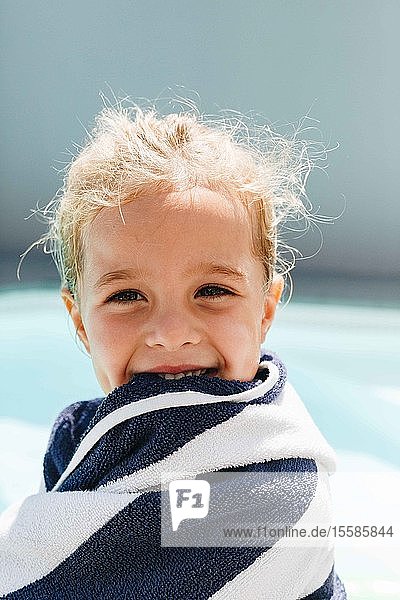 Happy little girl wrapped in towel by swimming pool
