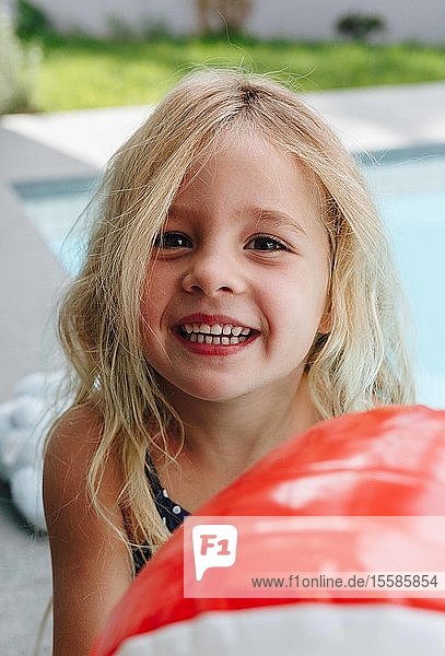 Glückliches kleines Mädchen mit Ball am Swimmingpool sitzend
