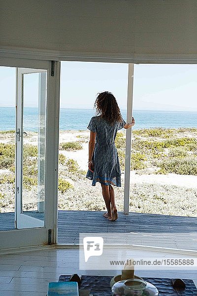 Frau genießt Meeresblick auf der Veranda des Strandhauses