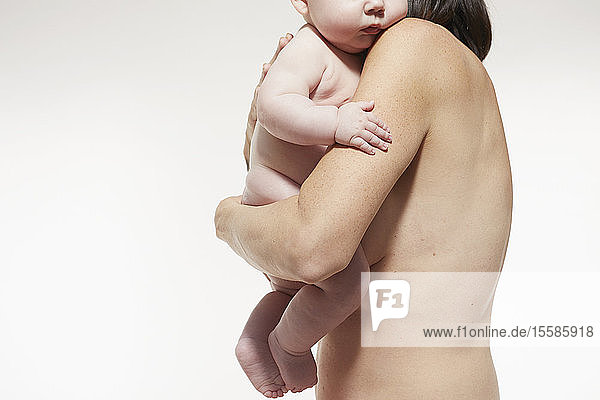 Naked mother comforting naked baby resting against her chest
