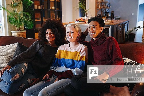 Happy mid adult man and young female friends watching tv on living room sofa