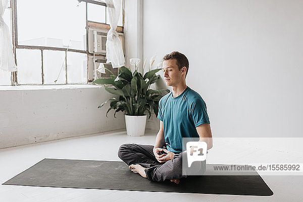 Mann sitzt in Lotus-Pose im Yoga-Studio