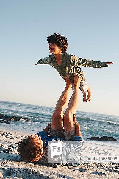 Vater hebt Sohn in der Luft mit Beinen am Strand