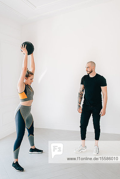 Fitness instructor observing woman lifting medicine ball in studio