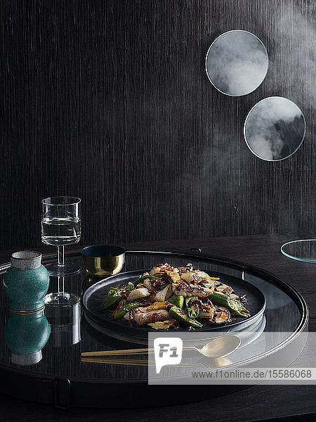 Rustic low key still life with plate of stir fry coral trout okra and xo sauce on tray