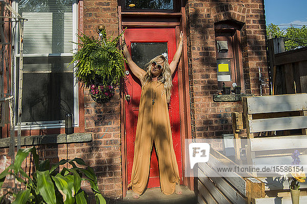 Mittelgroße erwachsene Frau posiert mit erhobenen Armen in der Türöffnung bei der Gartenparty der Gemeinde  Porträt
