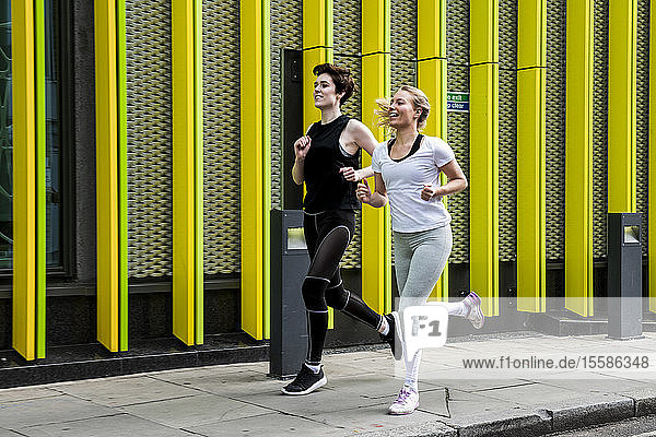 Zwei junge Läuferinnen laufen über den Bürgersteig der Stadt  in voller Länge
