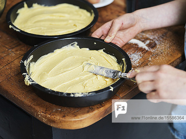 Mädchen beim Backen eines Kuchens  Glätten der Kuchenmasse in Kuchenform am Küchentisch  Nahaufnahme der Hände