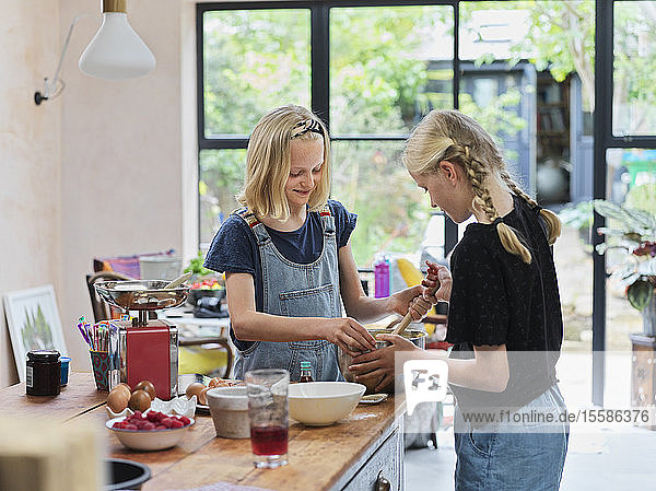 Mädchen und ihre Schwester backen einen Kuchen und rühren die Kuchenmasse in einer Rührschüssel am Küchentisch um